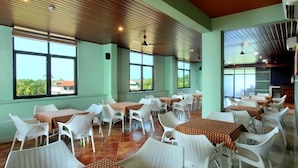 Un'ampia sala da pranzo interna con numerosi tavoli e sedie, ampie finestre e un soffitto alto con pannelli in legno.