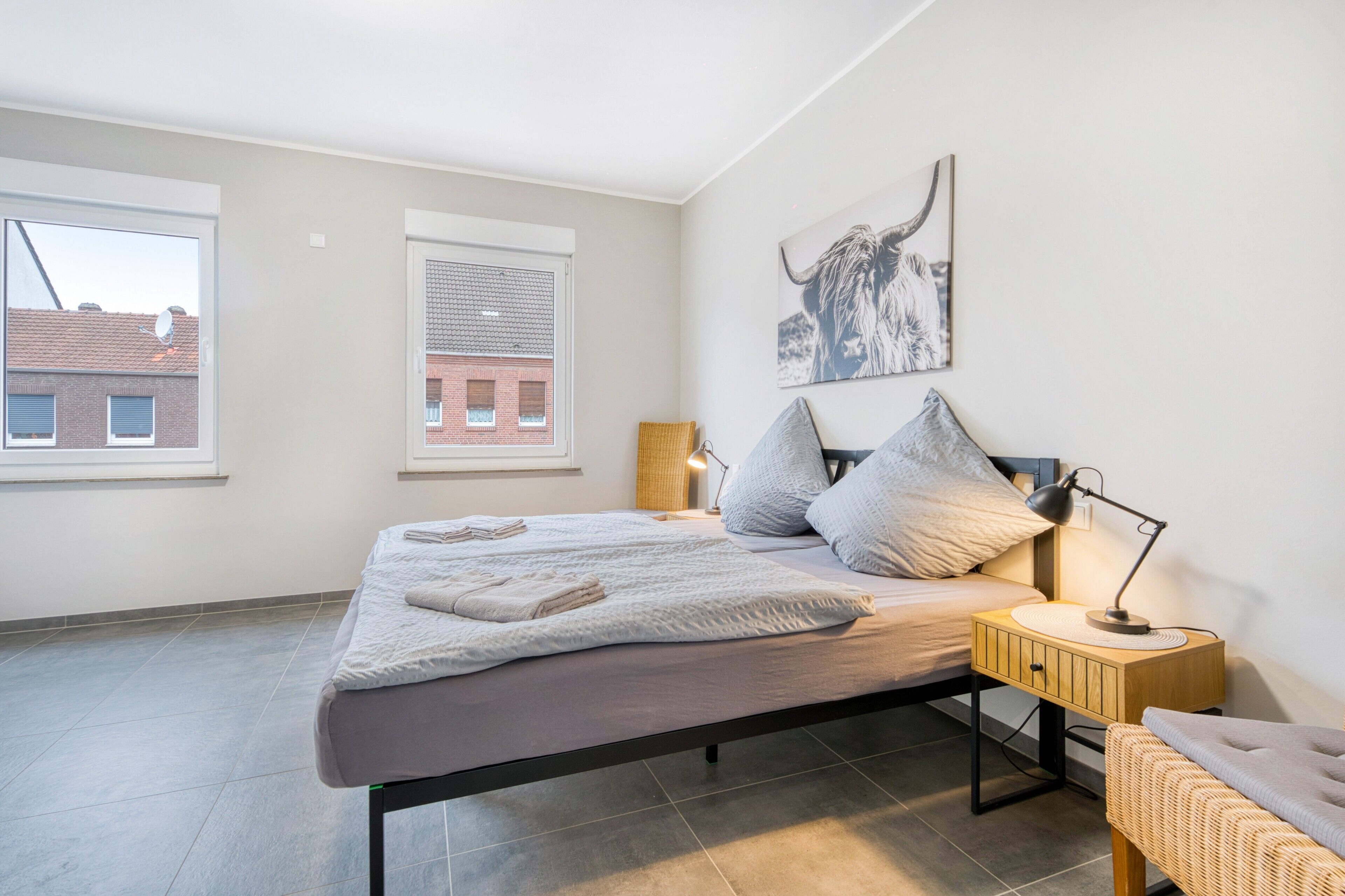 Een moderne slaapkamer met een bed, nachtlampjes, een raam en een aan de muur hangend kunstwerk.