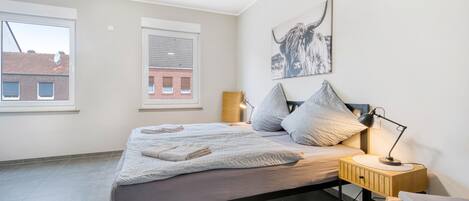 Een moderne slaapkamer met een bed, nachtlampjes, een raam en een aan de muur hangend kunstwerk.