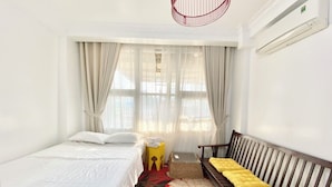 A bedroom with a bed, a bench with cushions, a small table, and a window with curtains. - Cherry Blossom Boutique Hotel NTMK (Ho Chi Minh City)