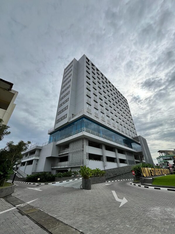 Um hotel de vários andares com design moderno, destacando uma entrada imponente com fachada de vidro e um céu claro ao fundo.