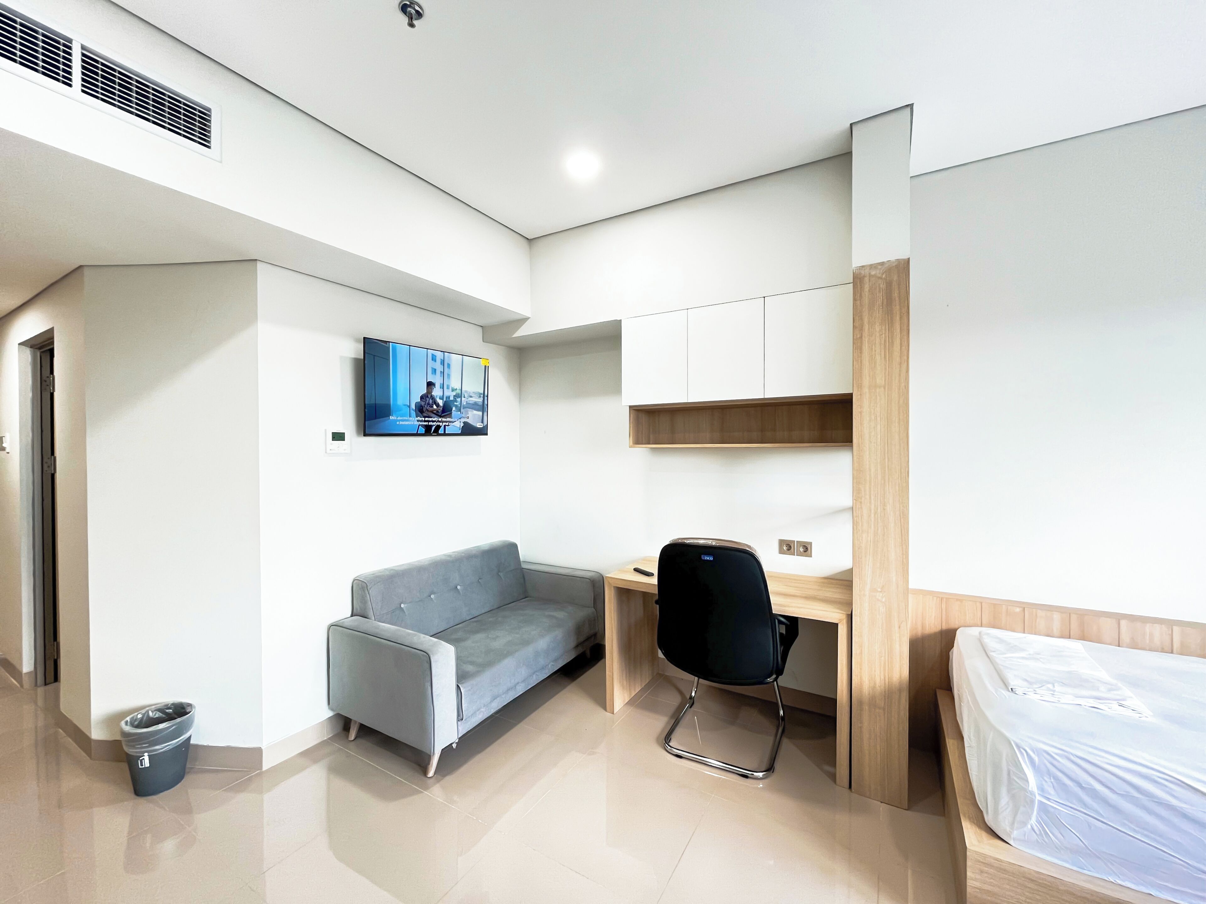 A modern bedroom with a bed, a desk, a sofa, and a TV mounted on the wall.
