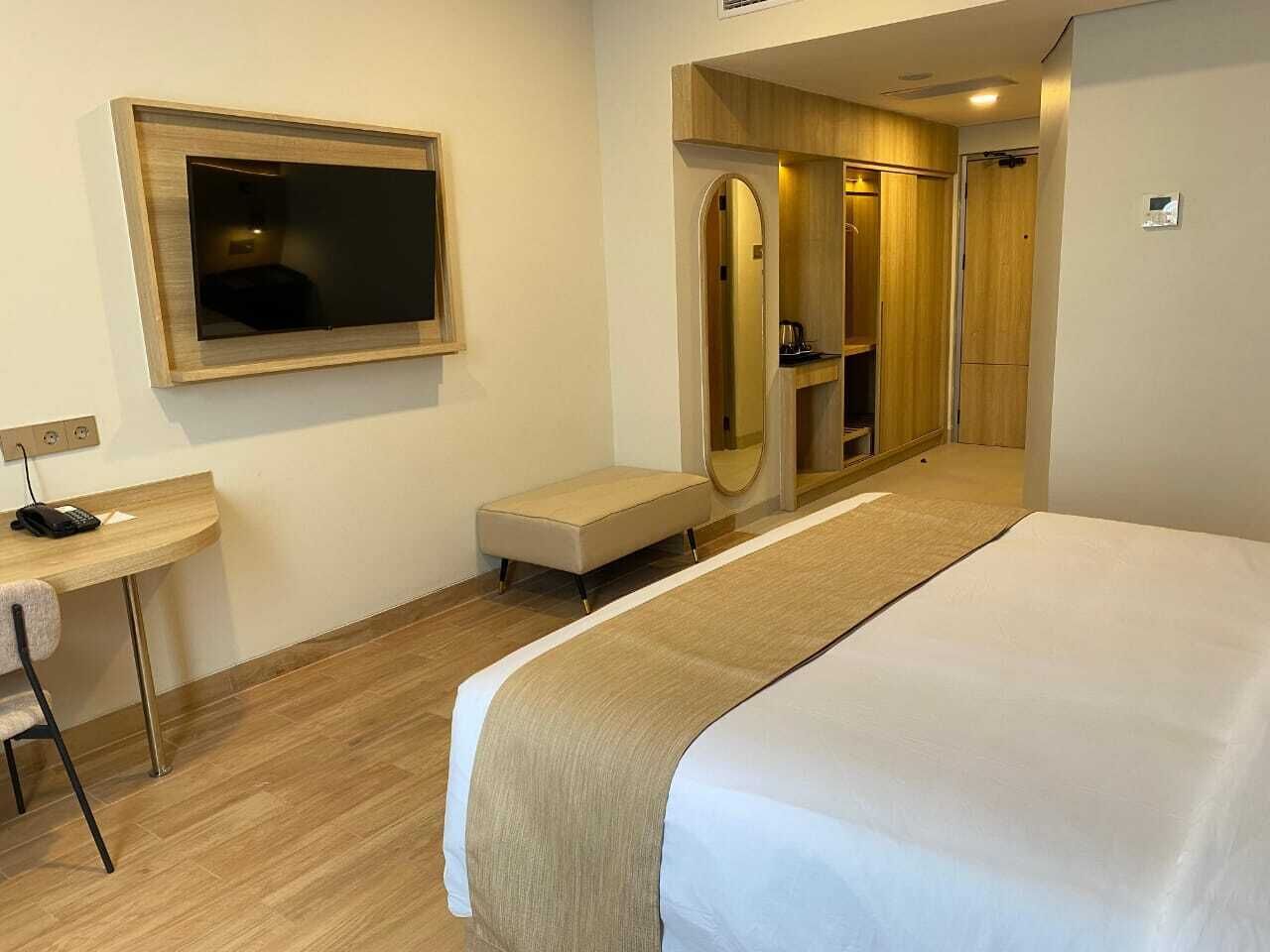 Habitación de hotel con una cama, un escritorio con silla, un espejo y un armario.