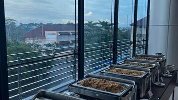 Un bufé con diversas opciones de comida, vistas a edificios a través de grandes ventanales y una decoración de diseño moderno.