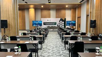 Un salón de conferencias con filas de mesas, sillas y una pantalla grande mostrando una presentación.