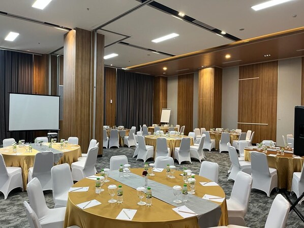 A conference room with multiple round tables, white chairs, and a projection screen.