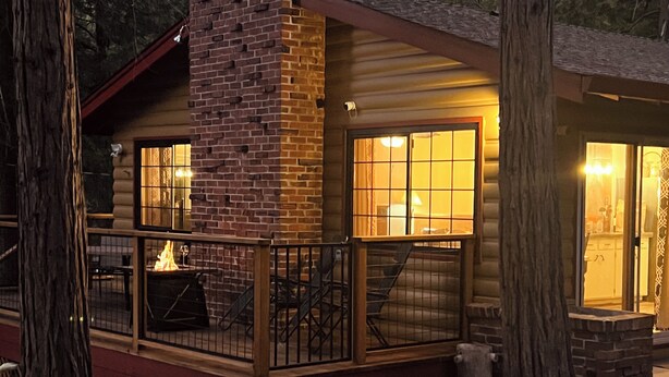 Une cabane dotée d’une terrasse en bois, d’une cheminée et d’une grande fenêtre.
