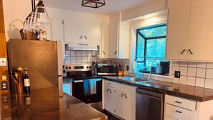 Une cuisine moderne avec des armoires blanches, une cuisinière en acier inoxydable, un lave-vaisselle et une fenêtre donnant sur des arbres.