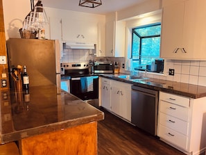 Eine moderne Küche mit weißen Schränken, einem Edelstahlherd, einer Spülmaschine und einem Fenster mit Blick auf Bäume.