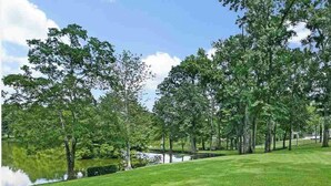 A well-maintained grassy area with trees and a calm water body, likely a park or garden setting.