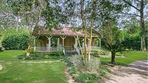 A single-story house with a porch, surrounded by a well-maintained lawn and mature trees.