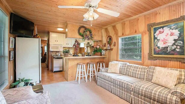 A cozy cabin interior with a kitchenette, a dining area with stools, a sofa, and a ceiling fan.