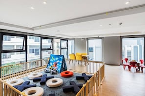 A spacious room with large windows, a play area with soft mats and a colorful mural, and a seating area with red chairs. - 2 Bed Room Central Location-sea View Infinity Pool (Pattaya)