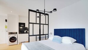Une chambre à coucher avec un lit, un lave-linge, une cuisine et une tête de lit bleue.