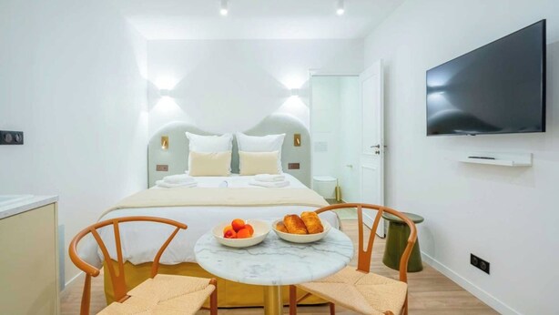A modern hotel room with a large bed, a flat-screen TV, a small round table with fruit, and two chairs. - Cosy studio - Hyper centre St Tropez (Saint-Tropez)