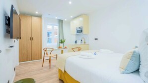 A hotel room with a bed, a desk, a chair, a small table with a plant, and a kitchenette. - Cosy studio - Hyper centre St Tropez (Saint-Tropez)