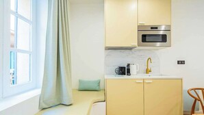 A compact kitchen with a built-in oven, a sink with a gold faucet, and a window with a curtain. - Cosy studio - Hyper centre St Tropez (Saint-Tropez)