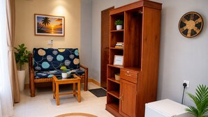 Un salon comprenant un canapé, un meuble en bois, une petite table, un réfrigérateur et un tableau accroché au mur.