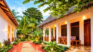Un hôtel doté d’une structure à toit de chaume, d’un espace extérieur couvert aménagé en coin salon et d’un sentier bordé de plantes et de galets.