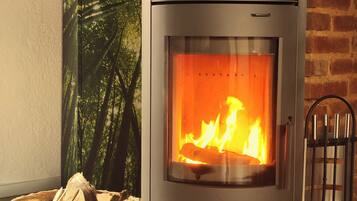 Un poêle à bois avec une flamme visible, un panier de bois de chauffage et un mur de briques en arrière-plan.