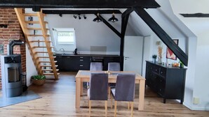 A loft-style kitchen with a brick wall, wooden staircase, and a dining area with a table and chairs. - Lovingly converted 90 sqm attic apartment. Experience idyllic Selfkant. (Heinsberg)