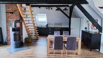 Une cuisine de style industriel, avec un mur en briques, un escalier en bois et un coin repas comprenant une table et des chaises.