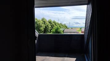 Une vue depuis une fenêtre, donnant sur des arbres et une éolienne au loin.