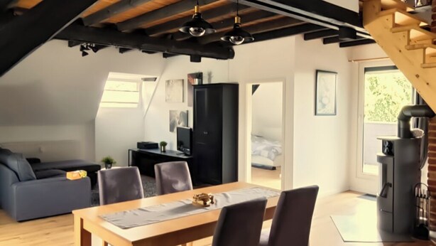 A modern loft-style living space with a dining area, a sofa, and a staircase. - Lovingly converted 90 sqm attic apartment. Experience idyllic Selfkant. (Heinsberg)