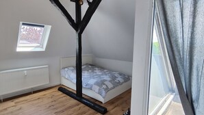 A small bedroom with a bed, a window, a radiator, and a wooden floor. - Lovingly converted 90 sqm attic apartment. Experience idyllic Selfkant. (Heinsberg)