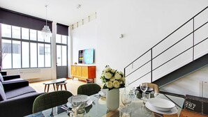 A modern dining area with a glass table set for four, a vase of white flowers, and a staircase with a railing.