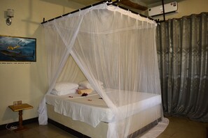 A bed with a white canopy, a small bedside table, a wall-mounted light, and a painting of a diver with a whale. - Meremeta Lodge (Mafia Island)