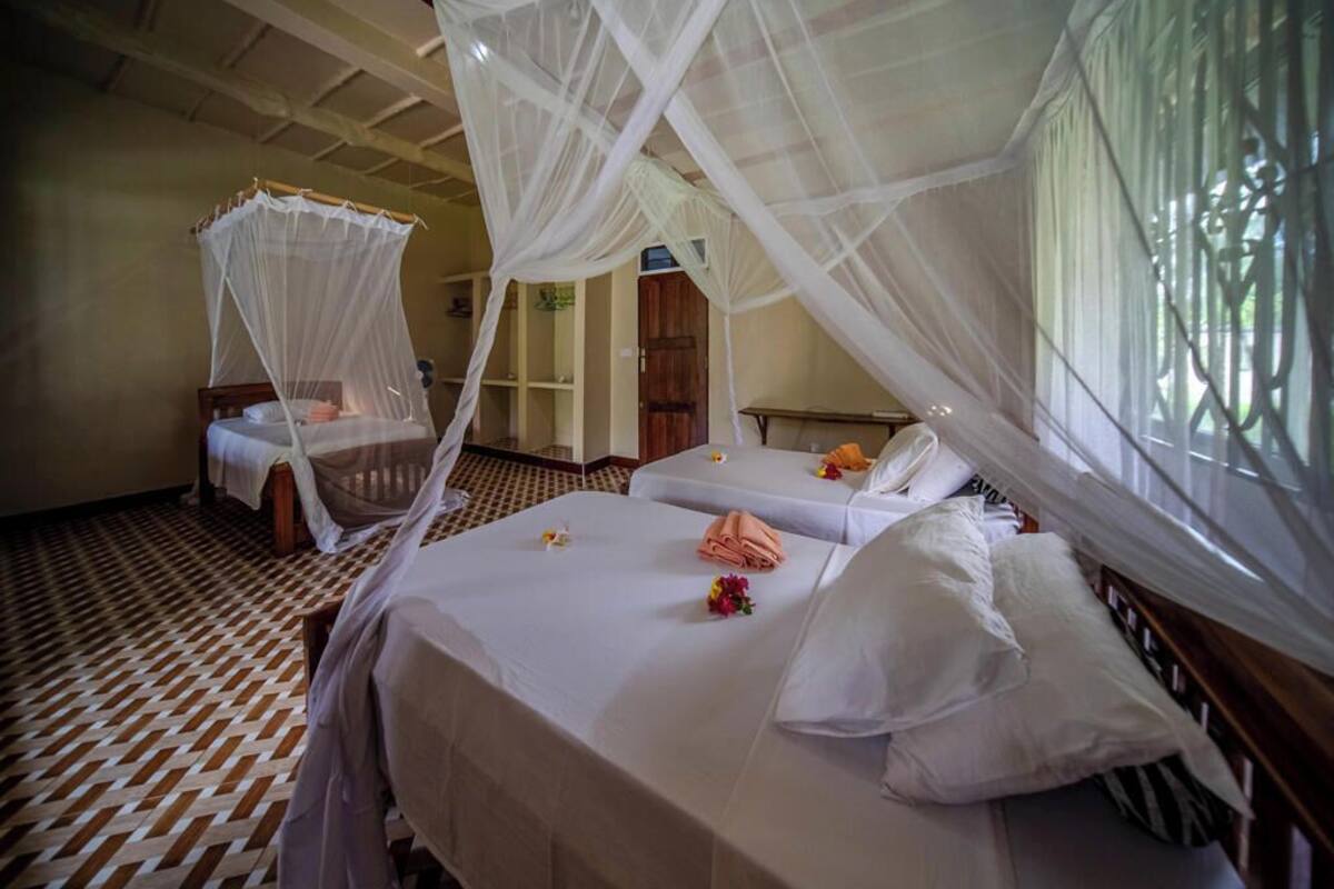 A room with two beds, each with a canopy bedspread and pillows. There is a patterned floor and a door in the background.
