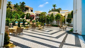 Een terras buiten met loungezetels en tafels, omgeven door palmbomen en een betegelde vloer.