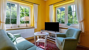 A room with yellow walls, a flat-screen TV, two armchairs, a sofa, a small table, and large windows with curtains. - Apartment '7' with Wi-Fi (Neuenkirchen)