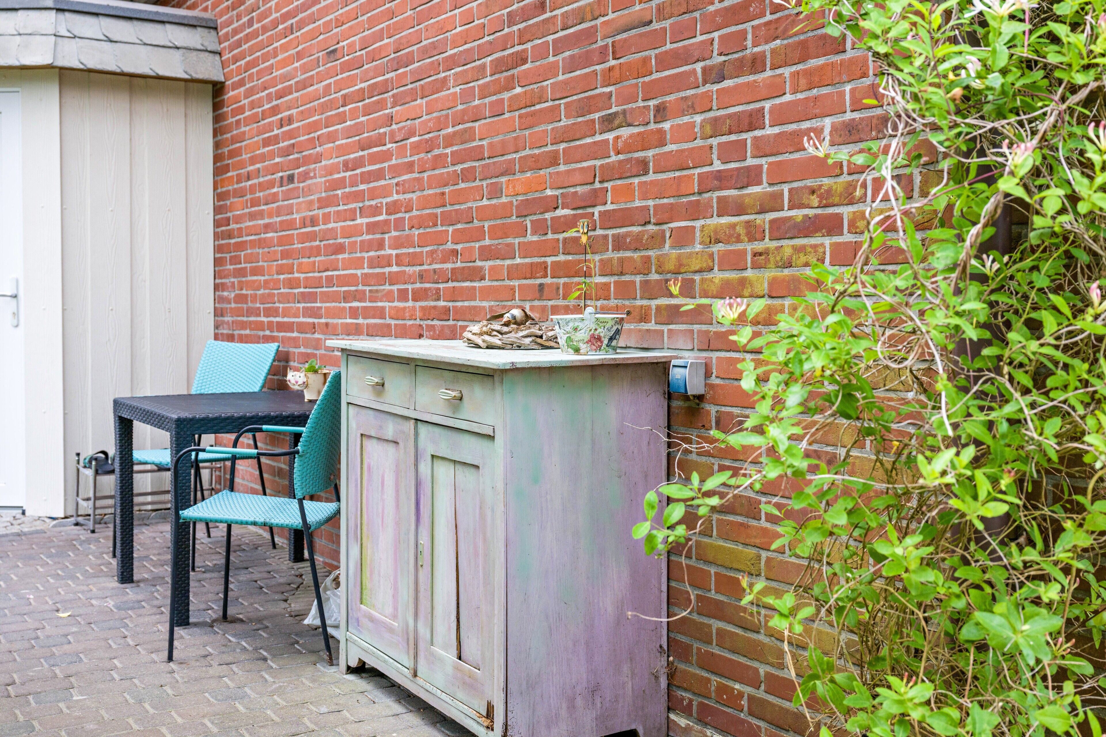 A brick wall, a blue chair, a table, and a cabinet with a plant on top.