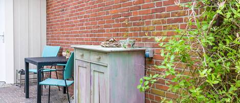 A brick wall, a blue chair, a table, and a cabinet with a plant on top.