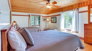 Une chambre avec deux lits, un plafond en bois, de grandes fenêtres avec des rideaux et un ventilateur de plafond.