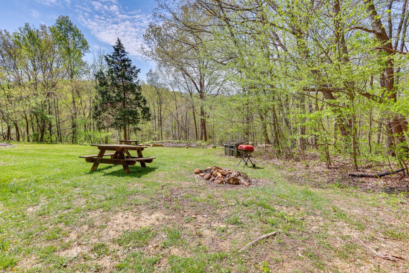 Un espace pique-nique équipé d’une table et de bancs en bois, entouré d’arbres et agrémenté d’un barbecue.