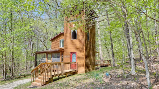 Une cabane en bois dotée d’un porche et d’une porte rouge, entourée d’arbres.