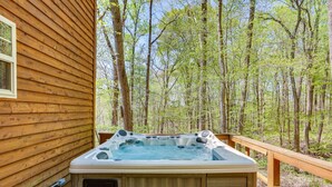 Une cabane en bois dotée d’un bain à remous sur une terrasse, le tout entouré d’arbres.