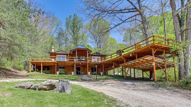 Une grande cabane en bois dotée d’un porche couvert et d’une terrasse au deuxième étage, le tout entouré d’arbres.
