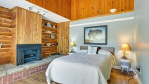 Une chambre avec un mur en bois, une cheminée, un lit et deux lampes de chevet.