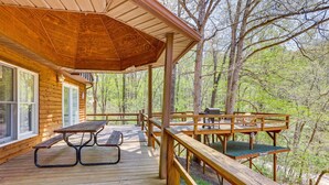 Une terrasse en bois avec des tables de pique-nique et un barbecue, entourée d’arbres.