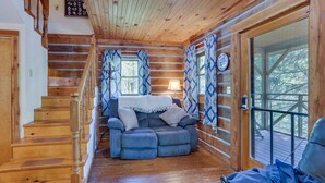 Ein rustikales Blockhaus-Interieur mit einer Holztreppe, einer Couch und Blick durch eine Glastür.