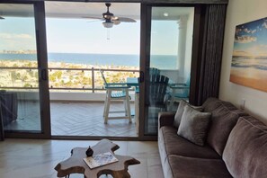 Un salon avec vue sur la mer, un ventilateur de plafond, un canapé, une table et une chaise.