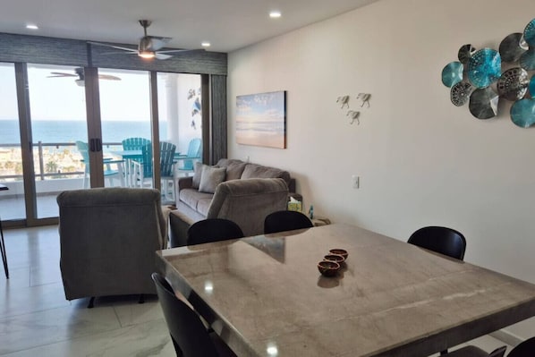 A dining area with a table and chairs, a sofa, and a view of the ocean through large windows.