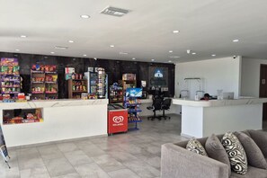 Een ruime lobby met een receptiebalie, een zithoek met een bank, en diverse snacks en dranken op schappen.