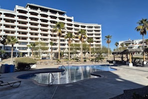 A hotel with a large pool area, palm trees, and a multi-story building with balconies.