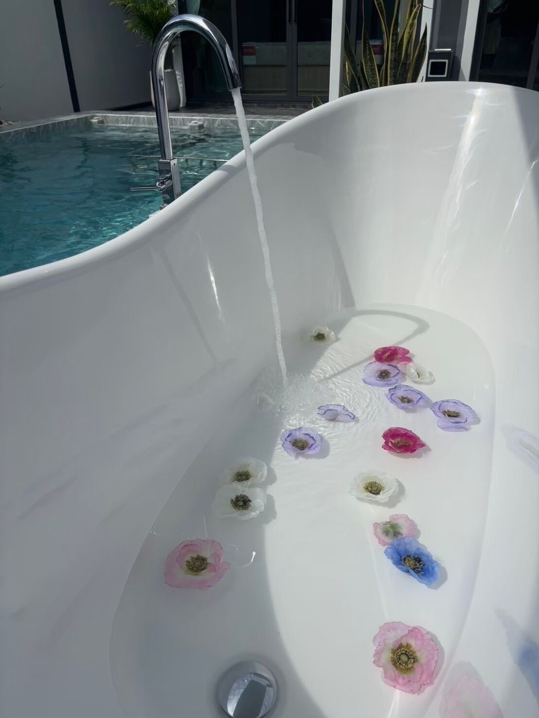 Une baignoire blanche remplie d’eau, entourée de fleurs flottantes.