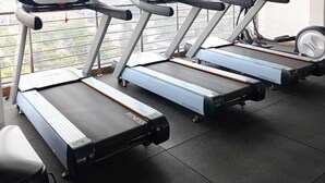 Three treadmill machines in a gym with a view of a cityscape through large windows.